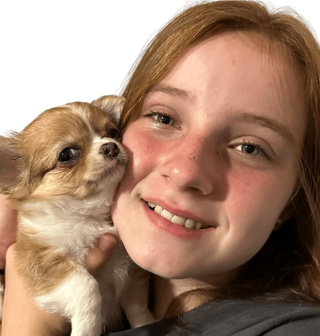 A girl smiling and holding a small dog close to her face.